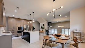 Una cocina moderna con una isla central, una mesa de comedor de madera e iluminación colgante.