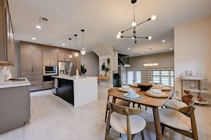 A modern kitchen with a central island, wooden dining table, and pendant lighting.