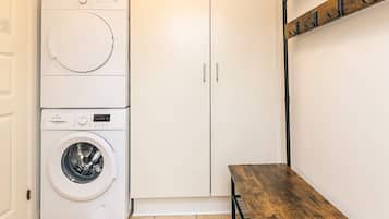 A laundry room with a stacked washer and dryer, a wooden bench, and a coat rack.