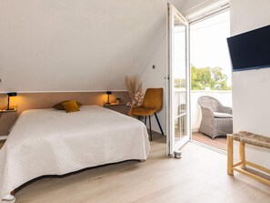 A bedroom with a bed, bedside lamps, a chair, and a view through a glass door to an outdoor seating area. - 5 Star Holiday Home in Brenderup Fyn (Middelfart)