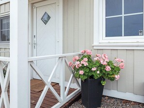 A white door with a diamond-shaped window, a black planter with pink flowers, and a white railing.