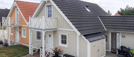 A two-story house with a balcony, a covered porch, and a patio area with a table and chairs.