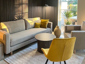 Un salon moderne avec un canapé gris, des coussins jaunes, une table basse ronde et un fauteuil jaune.