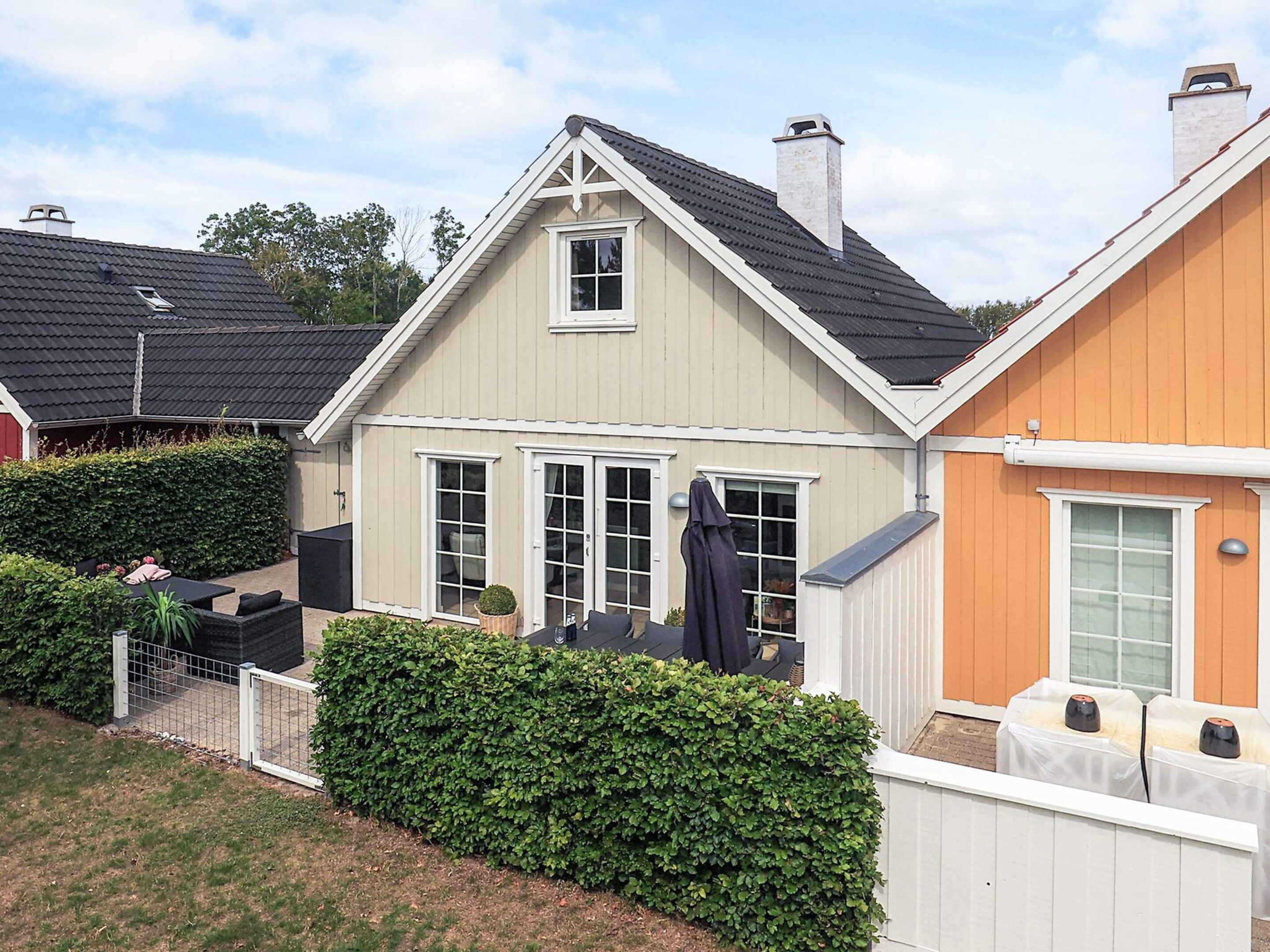 A two-story house with a sloped roof, a visible chimney, and a fenced backyard with a hedge.