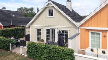 A two-story house with a sloped roof, a visible chimney, and a fenced backyard with a hedge.