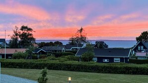 Un quartier résidentiel avec des maisons, un champ d’herbe et un coucher de soleil sur l’eau.
