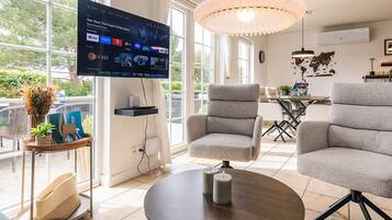 Una sala de estar moderna con una televisión de pantalla plana, sillones tapizados grises, una mesa redonda y una lámpara colgante.