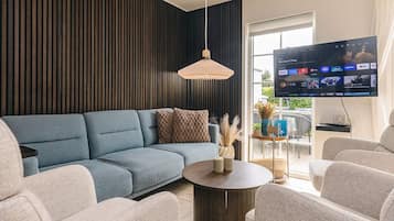 A modern living room with a sectional sofa, a round coffee table, and a flat-screen TV mounted on the wall.