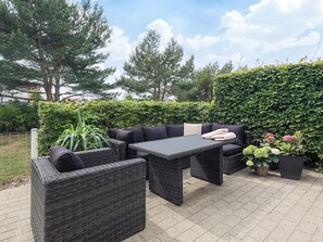 An outdoor patio area with wicker furniture, including a sofa and two armchairs, a rectangular table, and a potted plant.