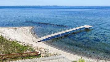 A pier extending into a calm sea, with a sandy beach and a wooden walkway leading to it.