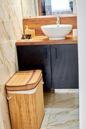 Un bagno con un mobile contenitore in legno, un lavandino bianco e un cestino in bambù.