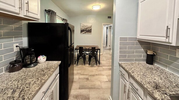 Una cocina con encimeras de granito, armarios blancos, un refrigerador negro y una zona de comedor con una mesa y sillas.