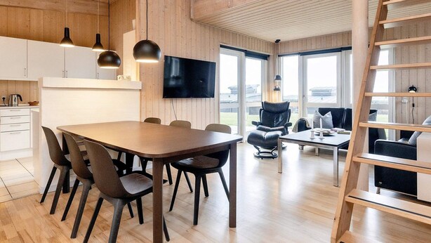 A modern interior with a wooden dining area, a black leather chair, and a TV mounted on the wall. - Well-maintained Holiday Home in Faborg (Faaborg)