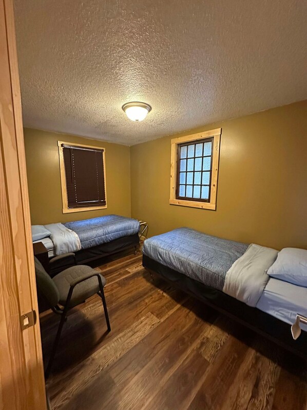A small, single-room accommodation with two single beds, a wooden floor, a ceiling light, and a window with a wooden frame. - Woodlands Retreat next to the Mississippi River (Alma)