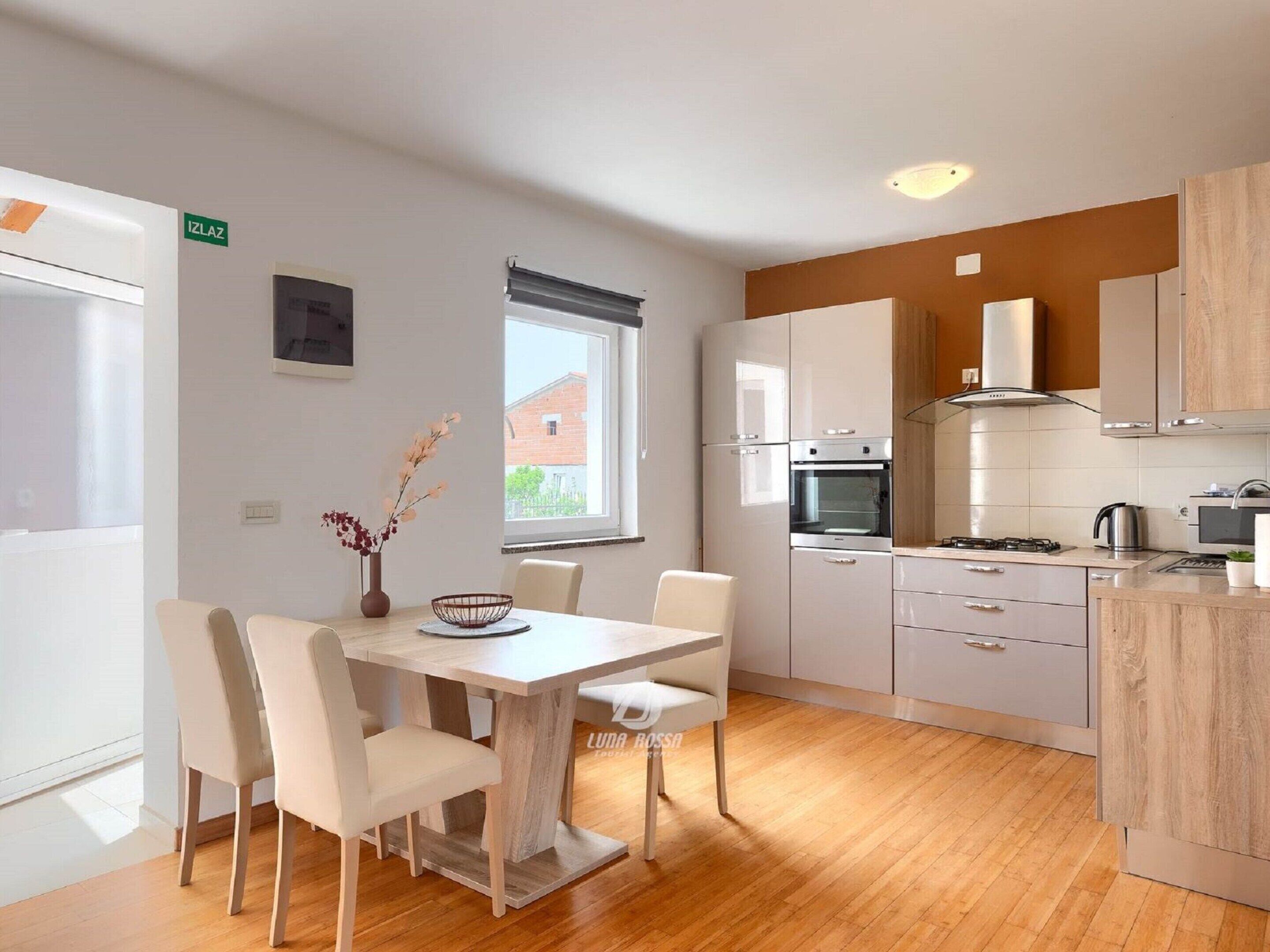 Une cuisine moderne avec des meubles blancs, une table à manger avec des chaises et une fenêtre qui laisse entrer la lumière naturelle.