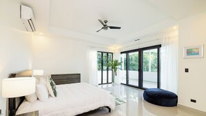 A modern bedroom with a bed, bedside lamps, a ceiling fan, and a view of the outdoors through large windows.