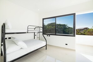 Een slaapkamer met een stapelbed, een groot raam en uitzicht op bomen en huizen.