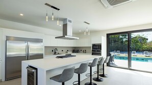 A modern kitchen with a large island, bar stools, and a view of a swimming pool.