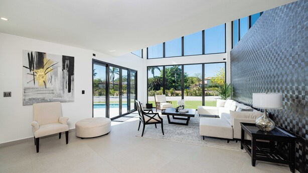 A spacious living room with a large window, a modern sofa set, a coffee table, and a painting on the wall.