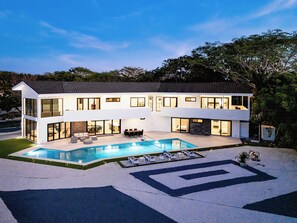 Een modern huis met twee verdiepingen, een zwembad, terras en een verzorgd gazon.