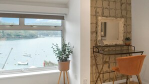 A room with a large window overlooking a body of water, a small table with a chair, and a decorative mirror on the wall. - 3 bedroom accommodation in Fowey (Fowey)