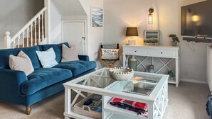A living room with a blue sofa, white coffee table, and a white console table with a lamp. - 3 bedroom accommodation in Fowey (Fowey)