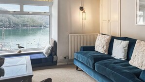 A cozy room with a view of a lake, a blue sofa with white cushions, a ladder outside the window, and a white radiator. - 3 bedroom accommodation in Fowey (Fowey)