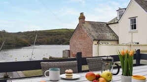A table with a bowl of fruit, two mugs, and a plate with pastries on a balcony overlooking a river. - 3 bedroom accommodation in Fowey (Fowey)