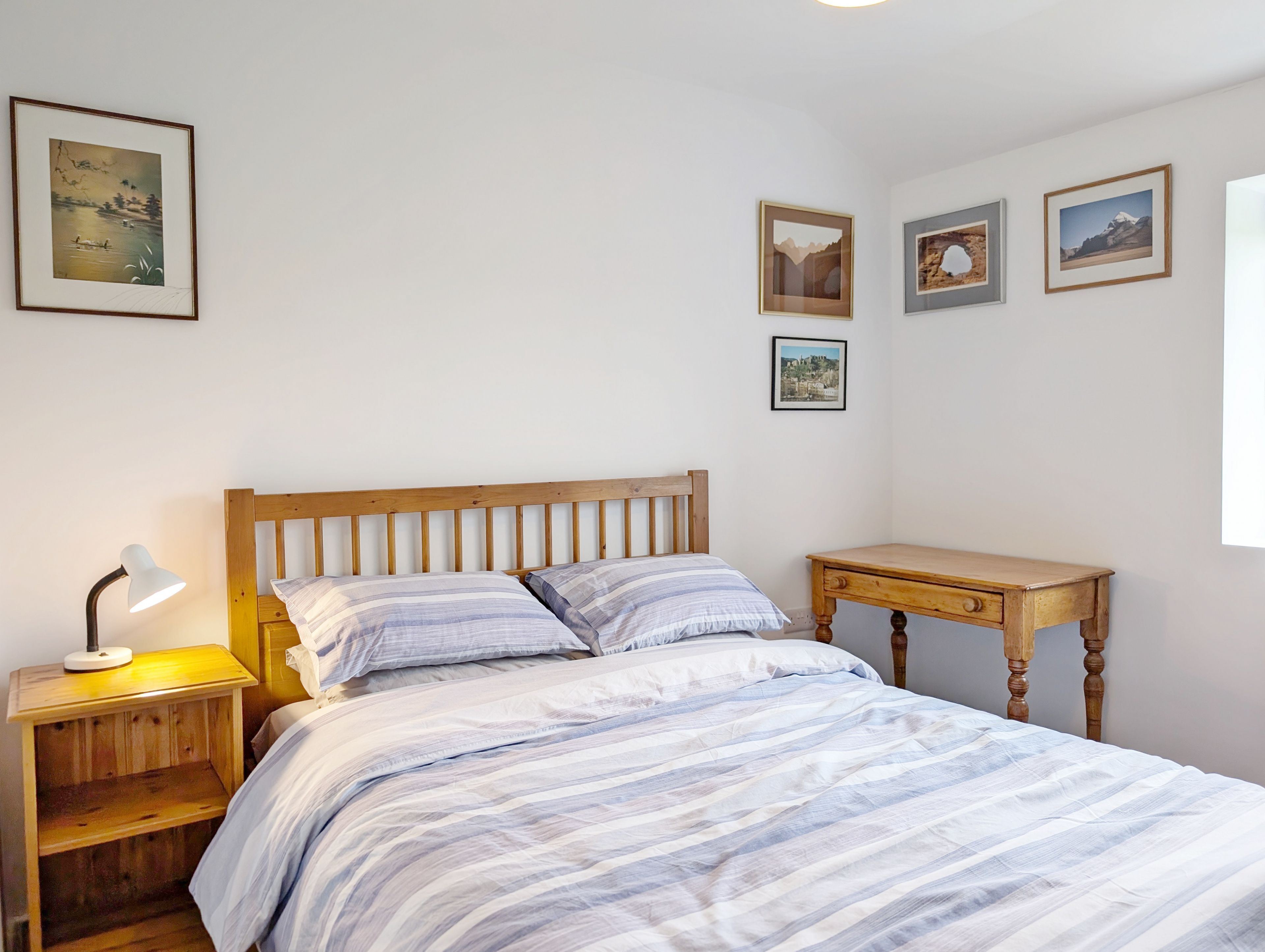 Un dormitorio con una cama de madera, una mesita de noche con una lámpara y una pequeña cómoda de madera.