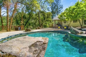 A clear swimming pool surrounded by trees, a covered patio area, and a house in the background. - Wine Country Retreat- Privacy-Spa/Pool/Games (Santa Rosa)