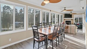 Un comedor espacioso con una gran mesa de madera y sillas, un ventilador de techo y ventanas amplias que ofrecen vistas al exterior.