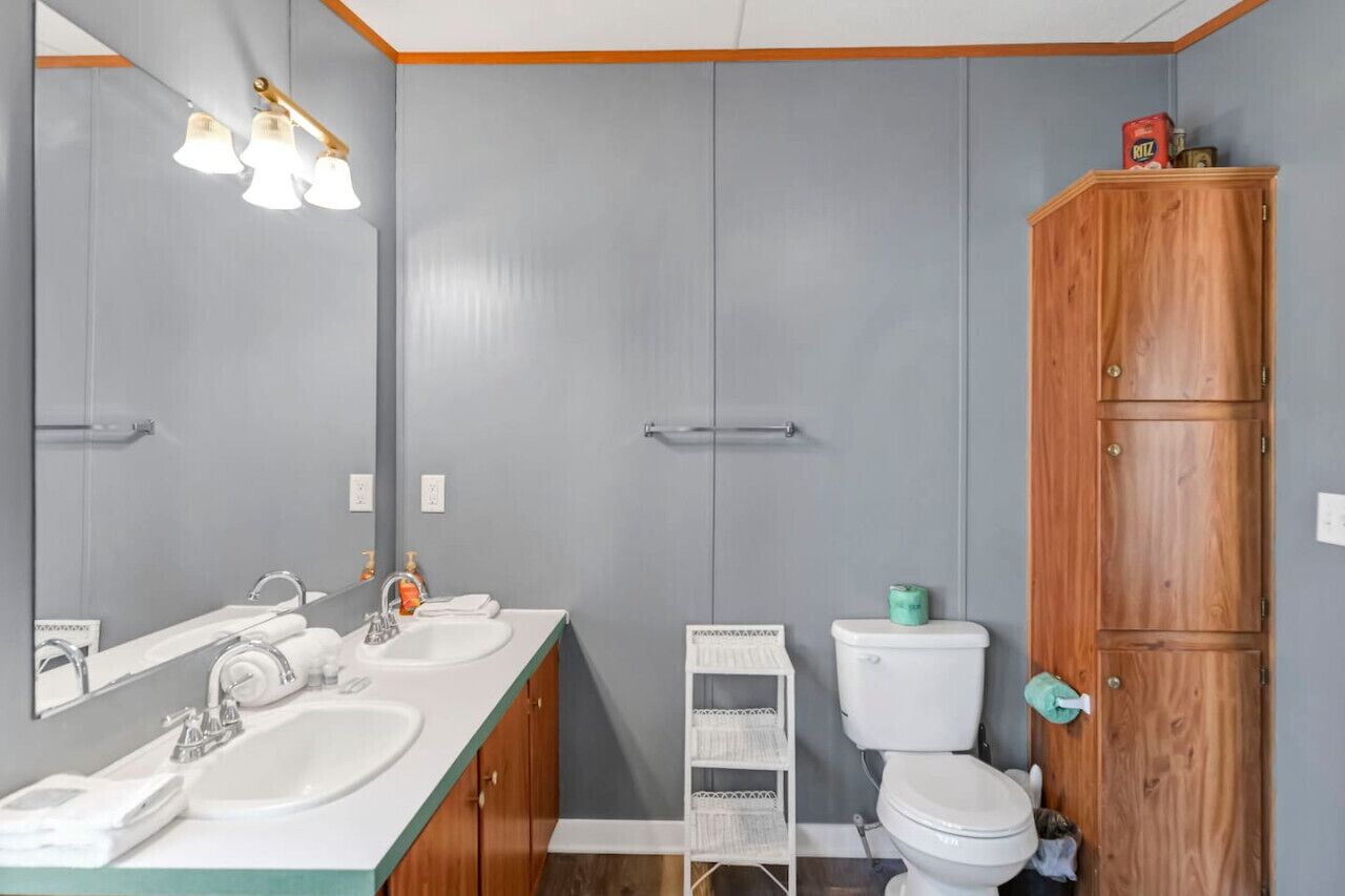 A bathroom with two sinks, a toilet, a cabinet, and a mirror.