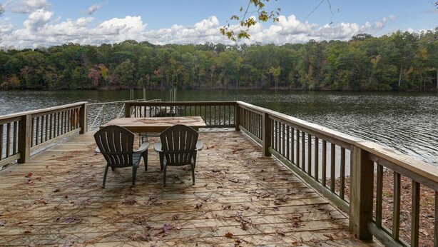 Terraza de madera con mesa y sillas que da a un lago, rodeada de árboles.