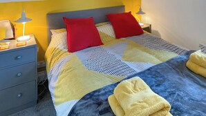 A neatly made bed with a patterned bedspread, two red pillows, and a stack of yellow towels on the floor. - 1 bedroom accommodation in Tregaron (Tregaron)
