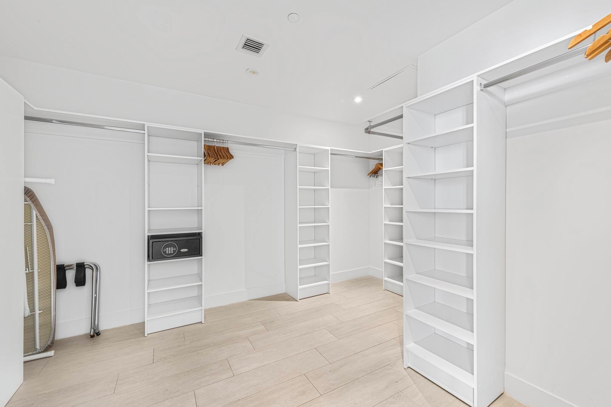 A modern, white interior with a walk-in closet featuring open shelving and a compact storage unit.