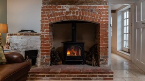 A brick fireplace with a wood-burning stove, a white stone mantle, and a brown leather sofa in the foreground.