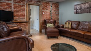 A living room with a brick wall, a television, leather sofas, and a glass coffee table.