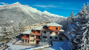 Un edificio a più piani con balconi, circondato da alberi e montagne innevate.