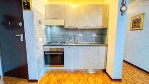 Una cucina compatta con piano cottura a gas, forno e lavello, mobili chiari e pavimento piastrellato.
