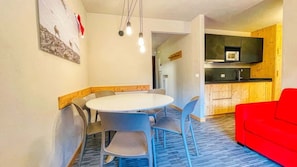 A dining area with a round table and chairs, a red couch, and a kitchen with wooden cabinets and a microwave.