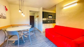 A compact living space with a dining area, a red sofa, and a kitchenette.
