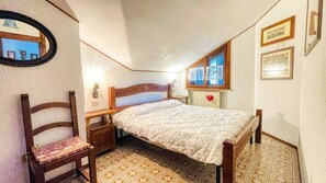 A bedroom with a bed, a chair, a nightstand, a window, and a radiator. - Appartamento Maison Des Alpes - Affitti Brevi Italia (Sauze d´Oulx)