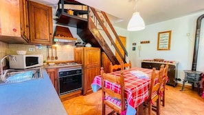 A kitchen with wooden cabinets, a microwave, an oven, a dining table with chairs, and a staircase.