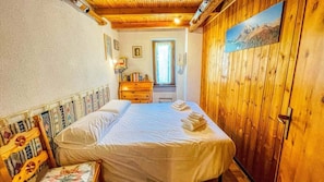 A bedroom with a wooden ceiling, a bed with white linens, a wooden dresser, and a window with natural light.