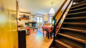 A cozy living room with a fireplace, a dining table with a red and white checkered tablecloth, and a staircase.