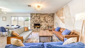 A modern living room with a stone fireplace, blue sofas, and a dining area with a table and chairs. - Oasis near STRIP-Lap Pool, Spa, Sauna, Poker, Deck (Las Vegas)