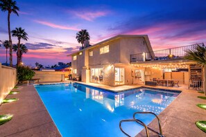 A modern two-story house with a swimming pool, outdoor seating, and palm trees.