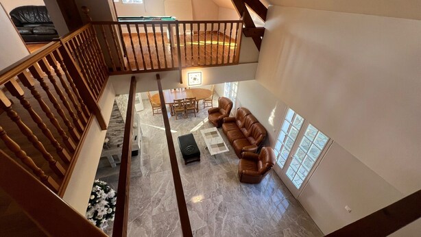 A spacious loft with a high ceiling, a wooden staircase, a dining area with a table and chairs, and a seating area with a sofa and ottoman. - Villa Le domaine des Rêves (Plateau d'Hauteville)
