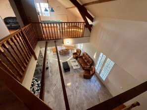 A spacious loft with a high ceiling, a wooden staircase, a dining area with a table and chairs, and a seating area with a sofa and ottoman. - Villa Le domaine des Rêves (Plateau d'Hauteville)