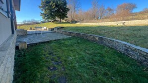 A stone patio with a stone wall, a grassy lawn, and a large tree. - Villa Le domaine des Rêves (Plateau d'Hauteville)